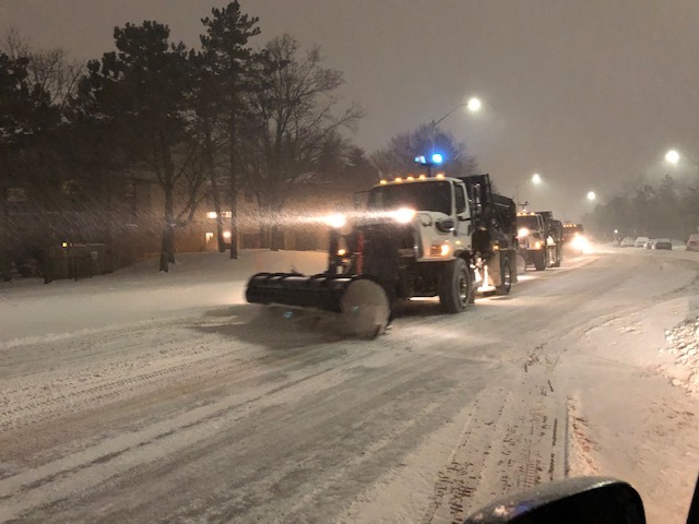 A snow plow clearing snow on a road in Mississauga at night.