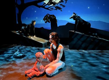 A person sitting down on stage handling a puppet.