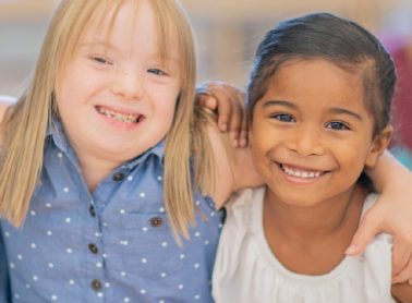 Two young girls standing side by side smiling.