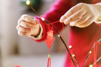 Close up of hands tying cultural symbol to a branch for Lunar New Year.