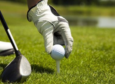 Close up of a person's hands wearing gloves putting a golf ball on a tee with a golf club beside it.