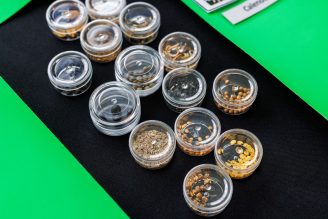 An arrangement of small clear containers, each filled with different types of seeds, displayed on a black cloth draped over a green table.