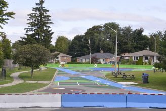 A colourful barricade separating the road way from the play area with homes in the back.