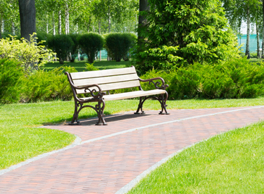 A park bench on pavement with a brick path.