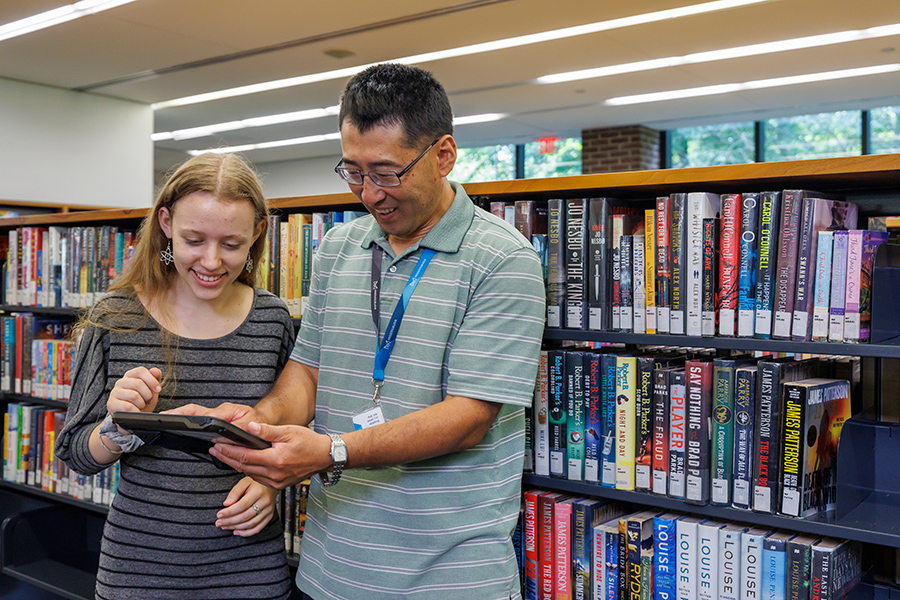 Two people using a tablet in front of library bookshelves