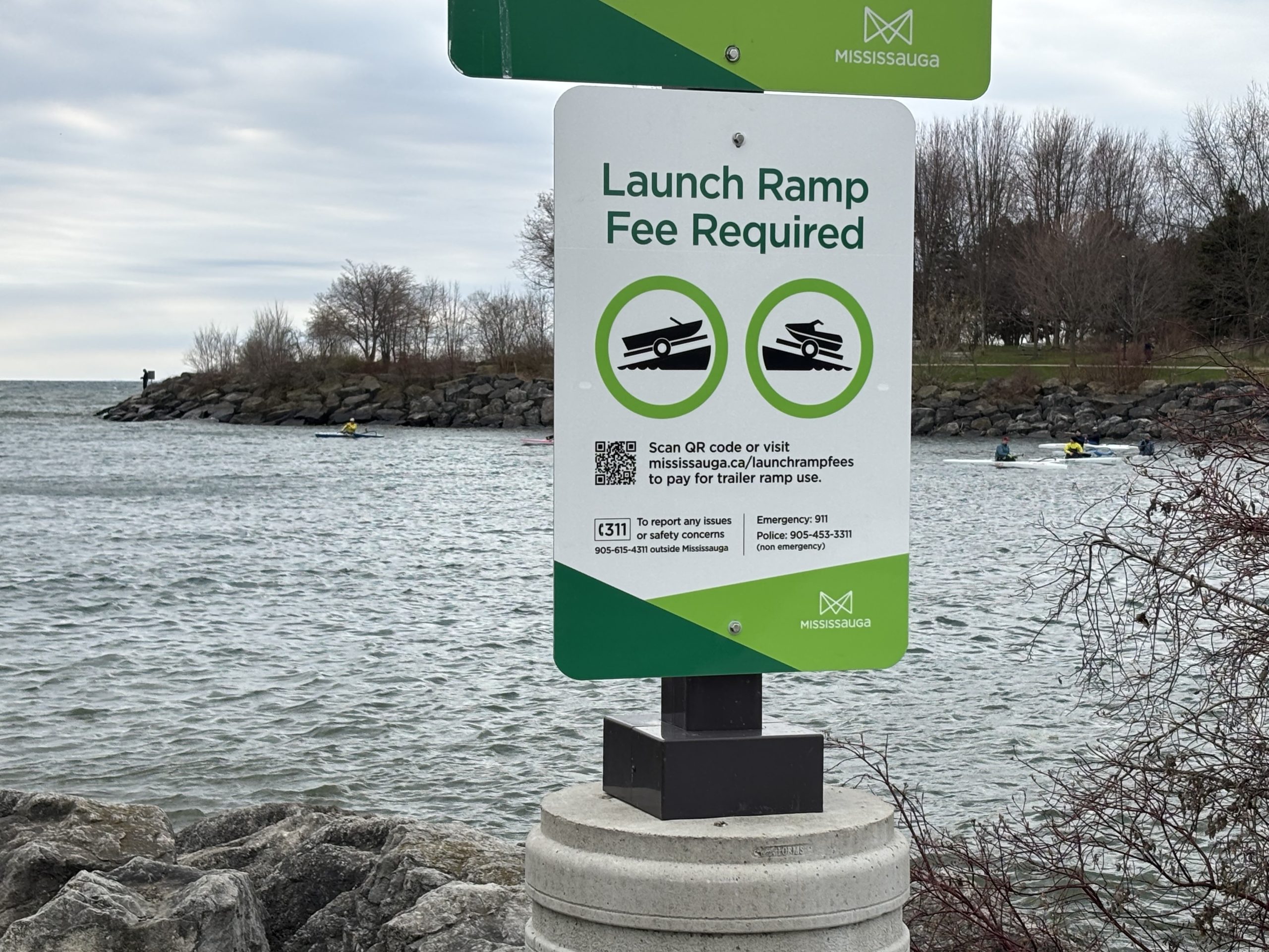 Signage installed at Mississauga waterfront launch ramp, with Lake Ontario in the background, that informs people that a launch ramp fee is now required to launch a watercraft from Mississauga's launch ramps. 