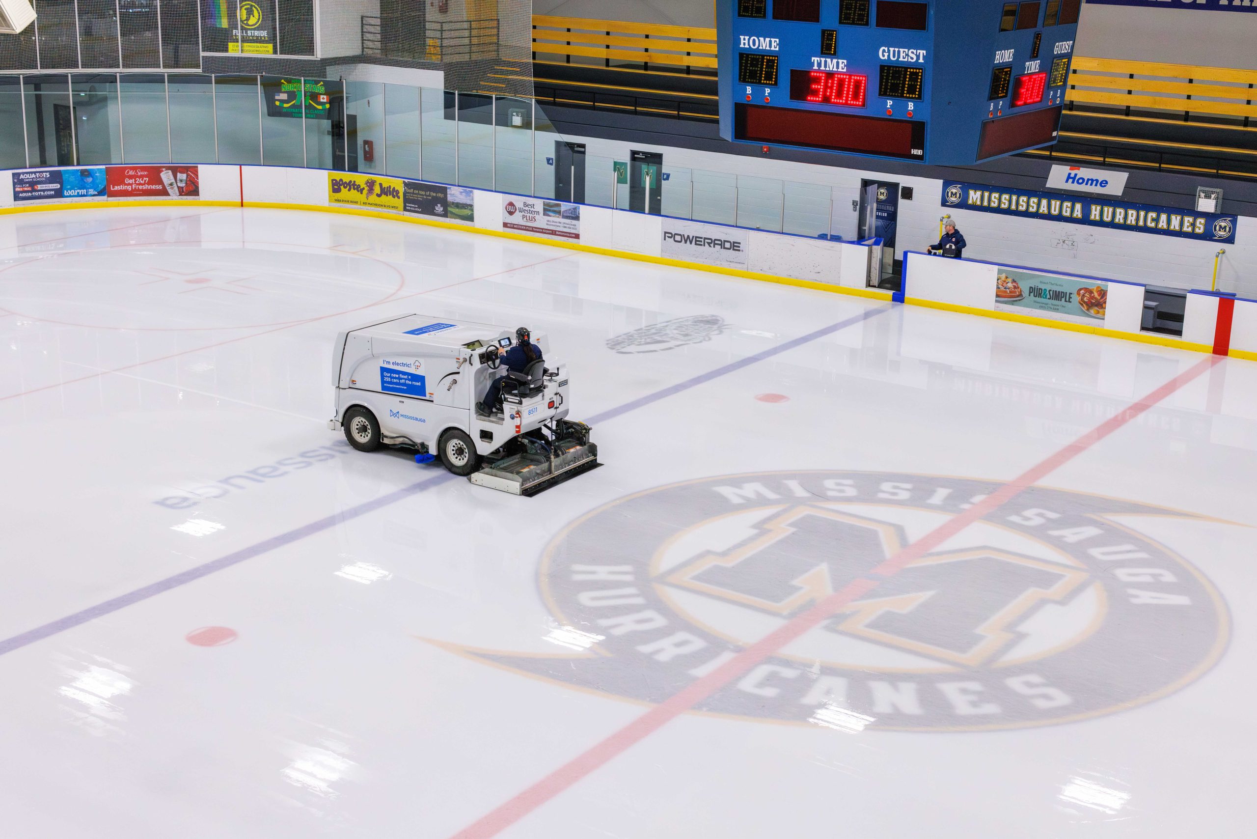 Ice resurfacing machine on a hockey rink with Mississauga Hurricanes logo at centre ice, showcasing multiple advertising elements.
