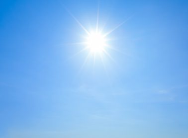 Shining sun with rays and clear blue sky background.