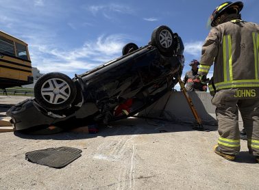 Firefighters lifting car up that is sitting on its roof.