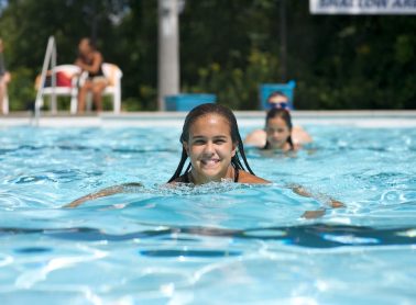 Girl swimming in an outdoor pool. Other swimmers in the background.
