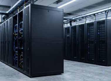 Rows of black server racks in a modern data centre, with visible network cabling and equipment in a data centre.