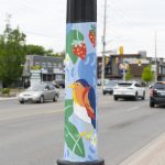 Painting of bird and strawberries on lightpost beside road.