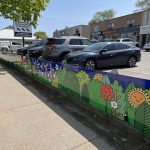 Artwork of trees, bushes, flowers and wind turbines on the retaining wall of a parking lot.