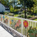 Painted pieces of wood depicting flowers, animals, people and trees affixed to a wrought-iron fence.
