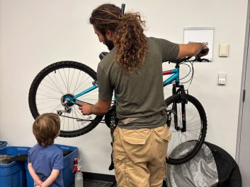 A volunteer is fixing a bike at a repair hub event while a young boy watches.