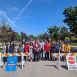 Staff, volunteers and dignitaries pose for a photo in front of one of the School Streets barriers.