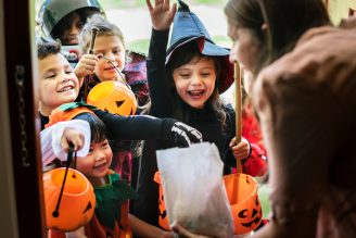 Several children reaching into a treat bag while wearing costumes.