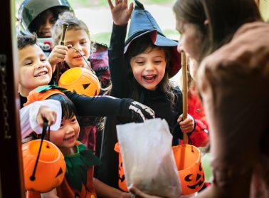 Several children reaching into a treat bag while wearing costumes.