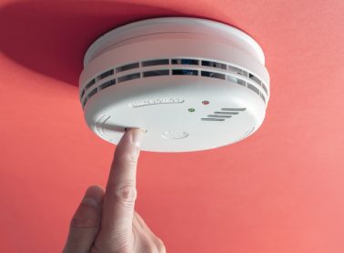 Home smoke and fire alarm detector maintenance man pushing button checking, testing or replacing battery