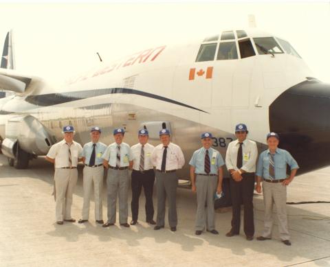 Photo of 8 employees wearing matching hats standing in front of an airplane