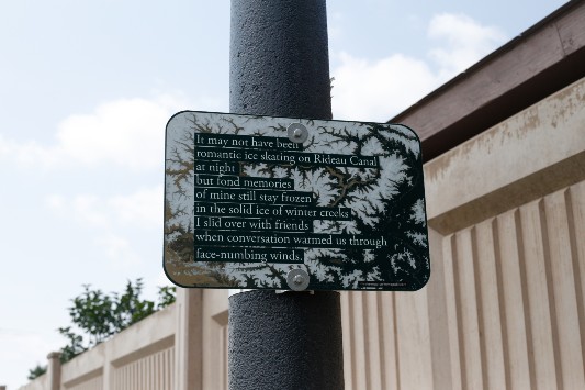 A sign on a light pole with lines of poetry.