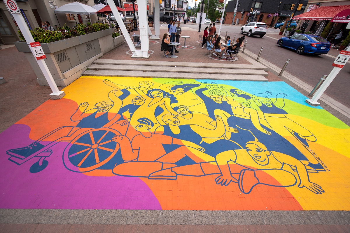 A painted mural on the ground with rainbow colours, depicting people dancing.