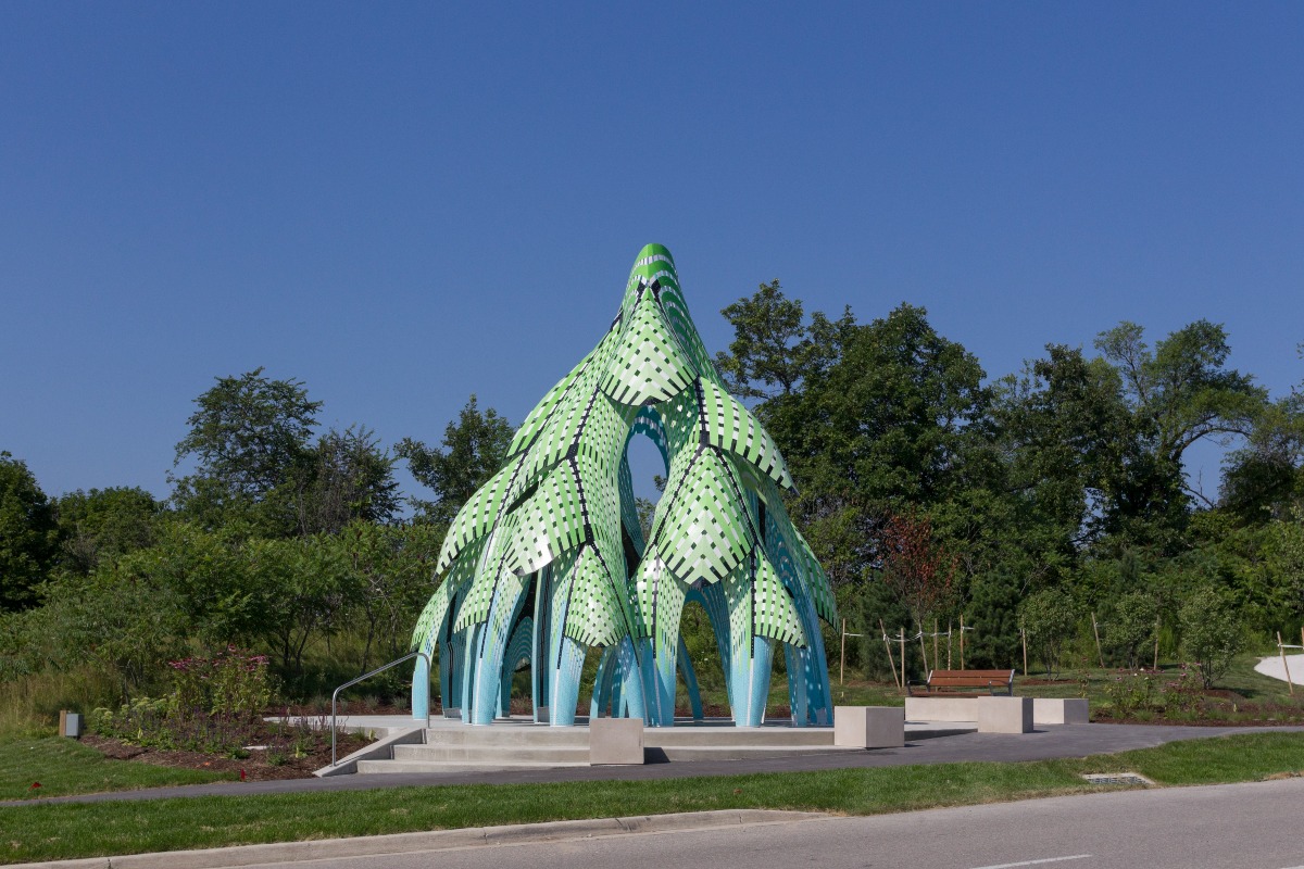 A large green and blue metallic sculpture in the shape of a pine tree.