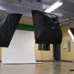 A photography studio with a white backdrop and 3 lighting softboxes.