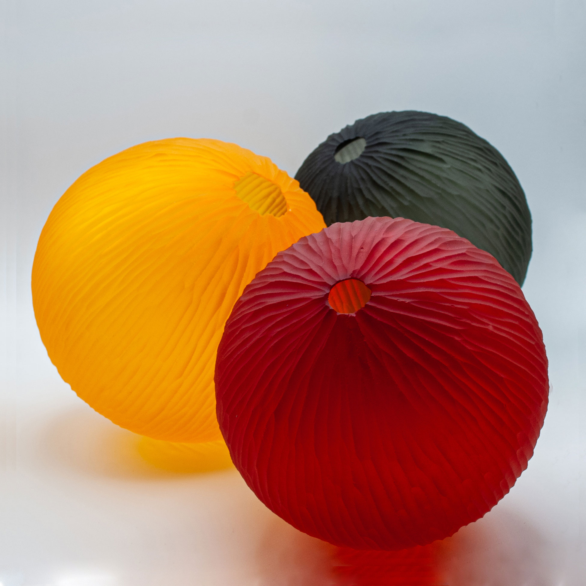 Three glass spheres in a row. One is yellow, one is red and one is black.