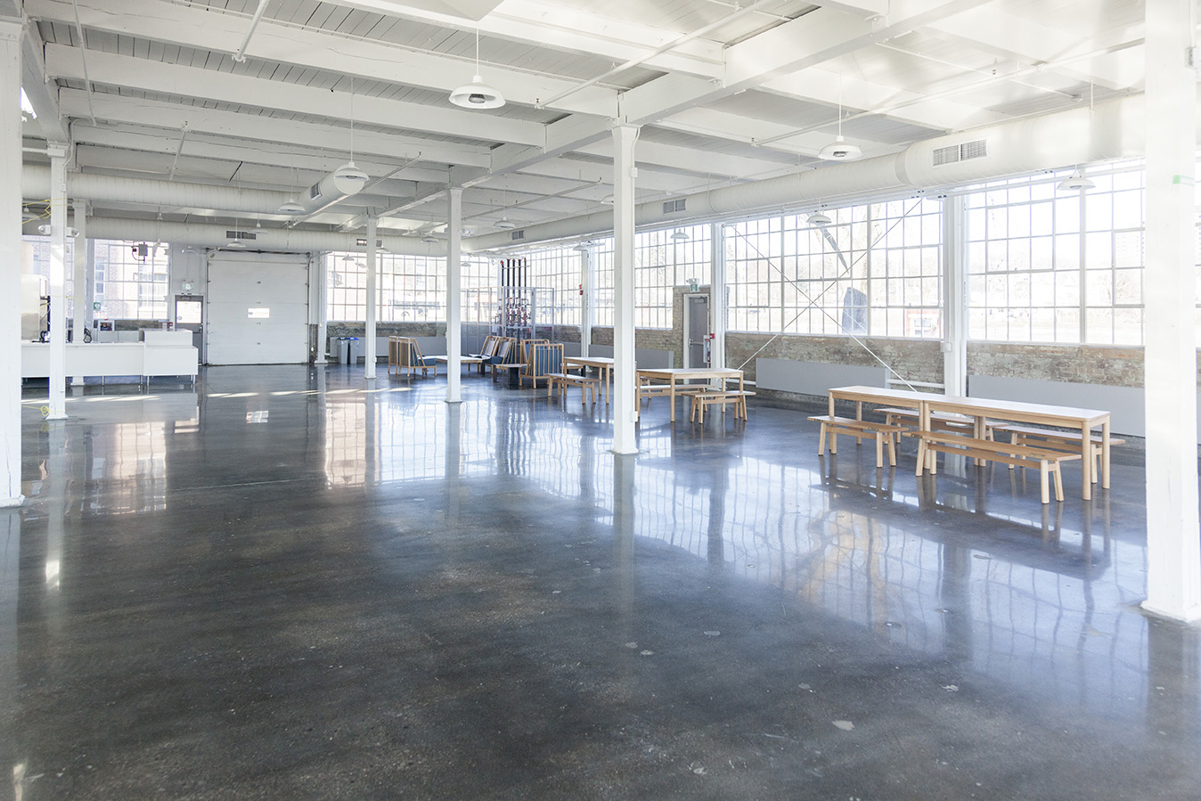 Brightly lit industrial space with rows of tables and chairs along one wall. CAPTION