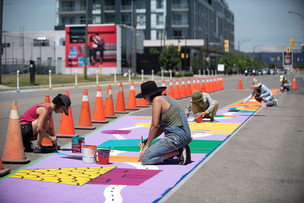Five artists painting a ground mural along a bicycle lane.