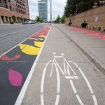 A ground mural painted along a bicycle lane that depicts pink and yellow abstract shapes.