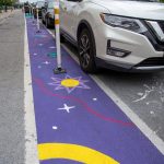 A ground mural painted along a bicycle lane that depicts cosmic elements like stars and planets.