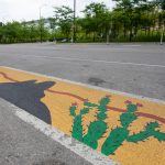 A ground mural painted along a bicycle lane that depicts cacti and desert landscape.
