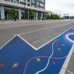 A ground mural painted along a bicycle lane that depicts stars and rainbows.