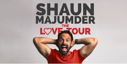 Comedian, Shaun Majumder, holding his hands behind his head with a large smile on his face. The text, Shaun Majumder Love Tour, appears in the background.