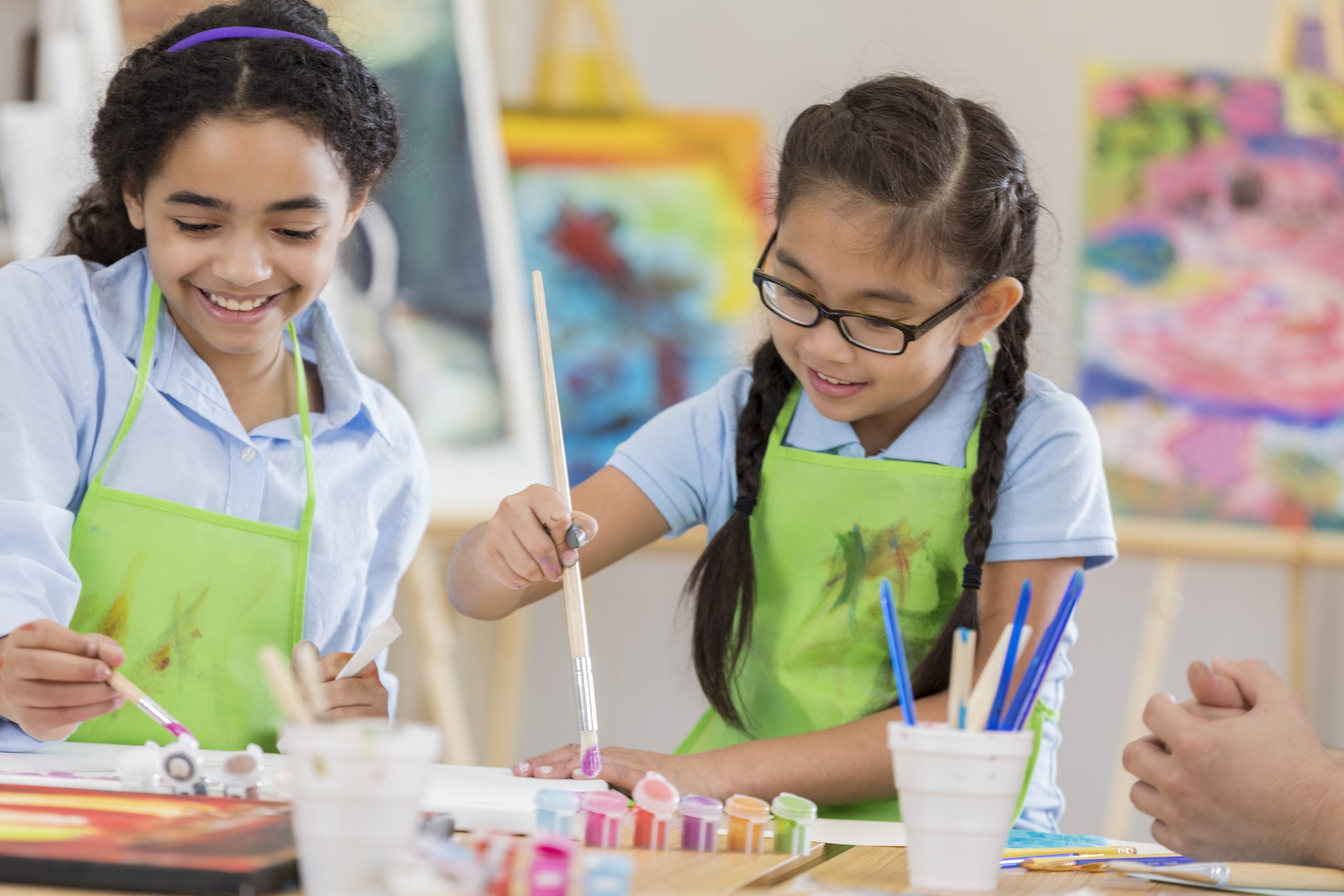 Two elementary school-aged students painting in a classroom.