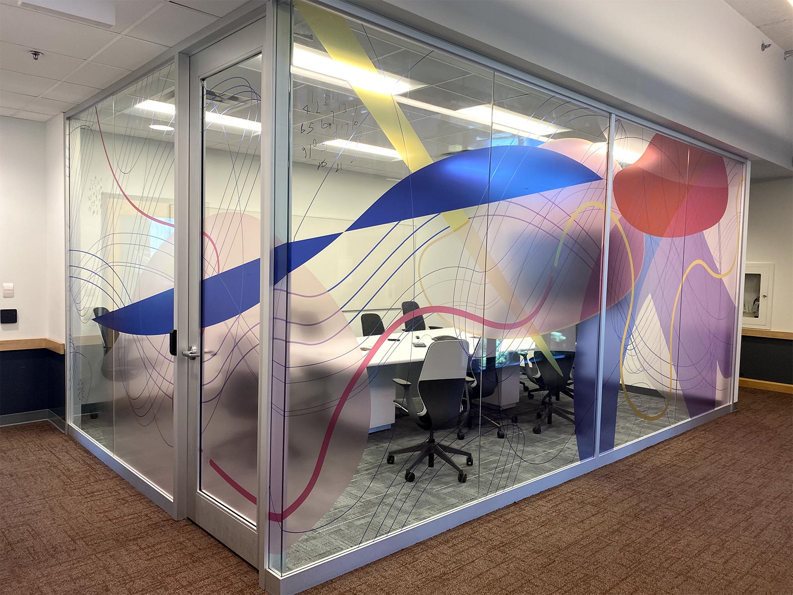 Glass panels with colourful pattern surrounding meeting area.