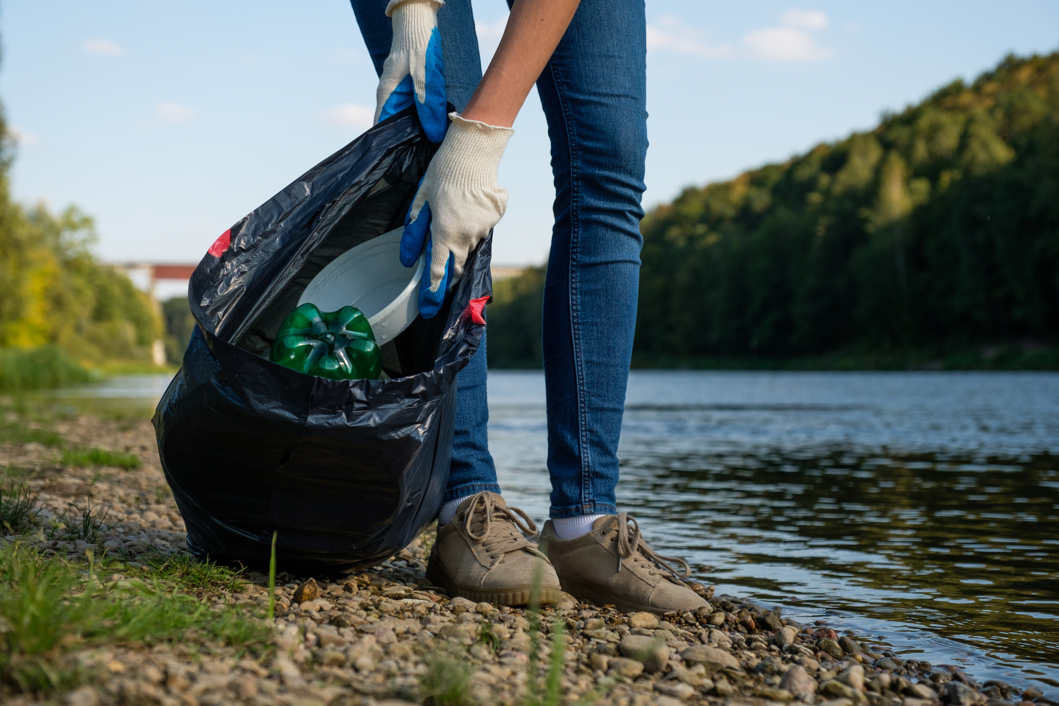 Volunteer woman collecting plastic rubbish on coast of a river