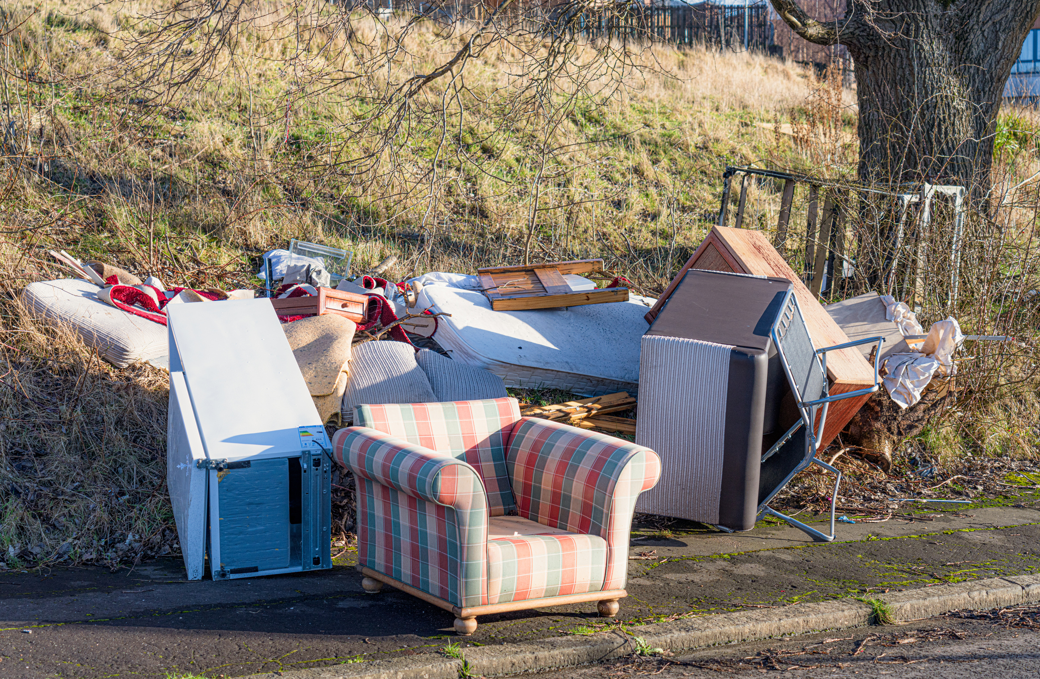 Unwanted household items left on the curbside, including an armchair, matress, fridge, cot and other items.