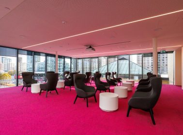 A photo of the Sky Reading Lounge. The carpet is bright fuchsia pink and there are black chairs and white coffee tables arranged in the space.