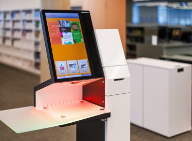 A height-adjustable self-checkout station with an illuminated screen.