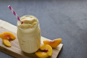 Peach milkshake in a glass jar with a straw
