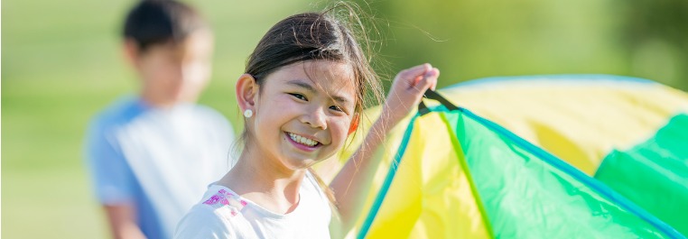 A girl playing with a parachute smiling at camera