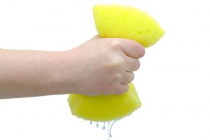Hand squeezing drip out of large yellow sponge on white background