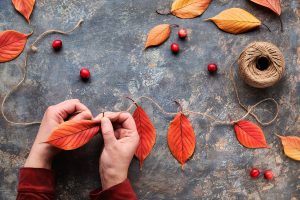 Fall DIY decorations from natural materials. Making garland with hemp cord and Autumn leaves.