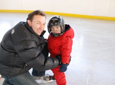 Man crouching down to help a toddler skate on the ice