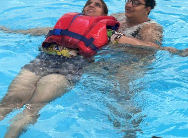 swim instructor teaching swim lesson to swimmer with life vest on