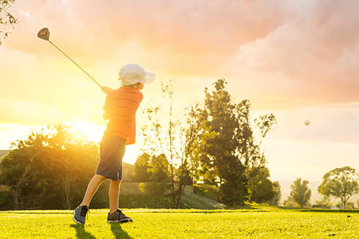 Child teeing off during a sunset.