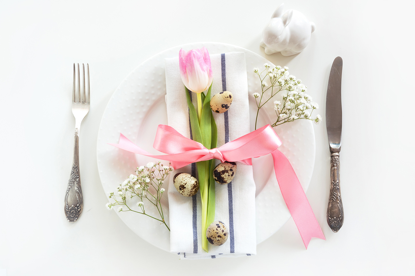Flat lay of a holiday table setting with golden cutlery, green porcelain plate and present on a gray table.